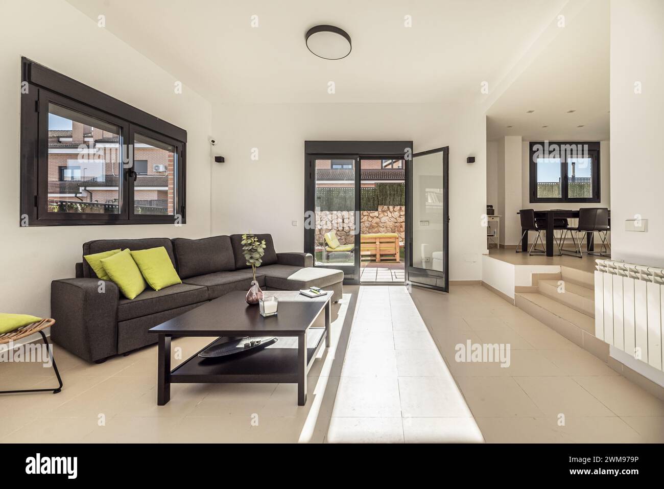 Wohnzimmer eines Einfamilienhauses mit glatten, weiß lackierten Wänden, Sitzbereich mit Chaiselonge mit grauen Stoffen und schwarzem Holzkaffee Stockfoto