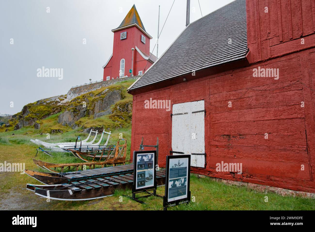 Ausstellung von Hundeschlittenarten im Sisimiut Museum, Grönland. Die „neue Kirche“ sitzt über der Szene auf einem felsigen Außenposten. Stockfoto