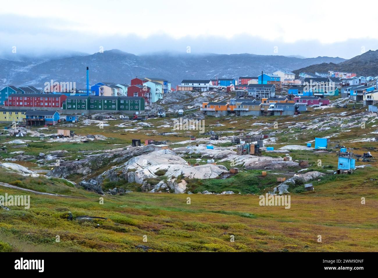 Wo die Schlittenhunde im Sommer leben, wenn sie in Illulisat, Grönland, arbeiten. Dahinter befinden sich einige hell bemalte Häuser von Illulisat Stockfoto