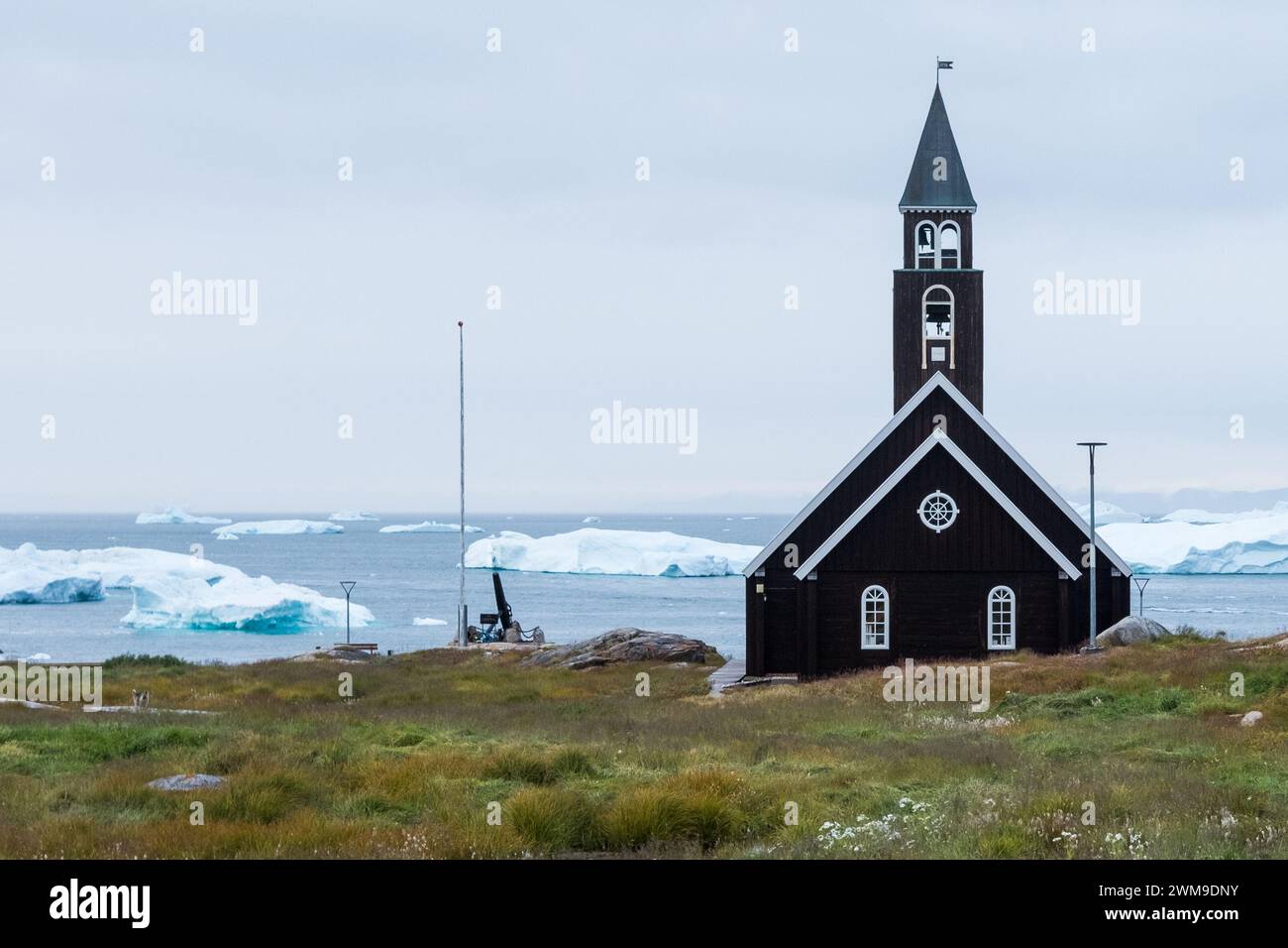 Zion's Church steht neben der Uferpromenade in Illulisat. Hinter schwimmenden Eisbergen, die vor kurzem vom nahegelegenen, massiven Eisfjord befreit wurden. Grönland. Stockfoto