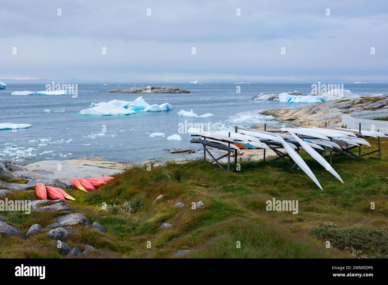 Neben einem Meer mit Eisbergen und Bergkugeln gibt es viele Kajaks. Einige sind im traditionellen Inuit-Stil - lang und schmal. Illulisat, Grönland. Stockfoto