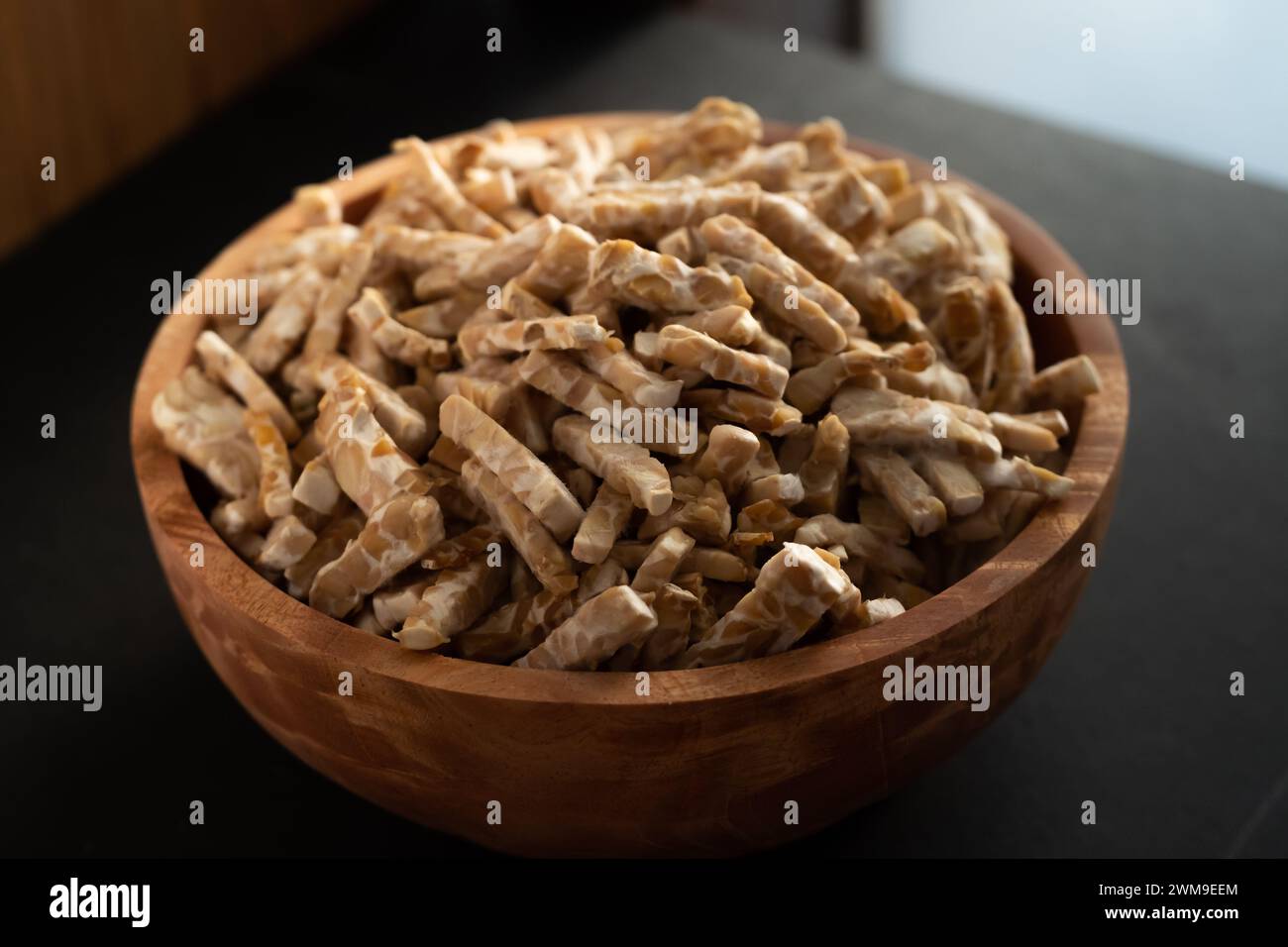 Tempe ist ein traditionelles indonesisches Essen aus fermentierten Sojabohnen. ​​tempeh in eine Holzschüssel geschnitten. Nahaufnahme, dunkler Holzhintergrund. Stockfoto