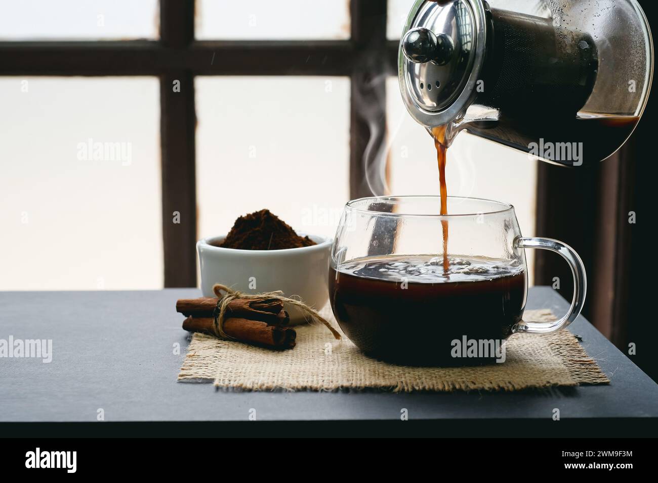 Zubereitung und Eingießen von heißem Kräuterkaffee in eine Tasse mit Dampf im Retro-Stil auf dem Tisch Stockfoto