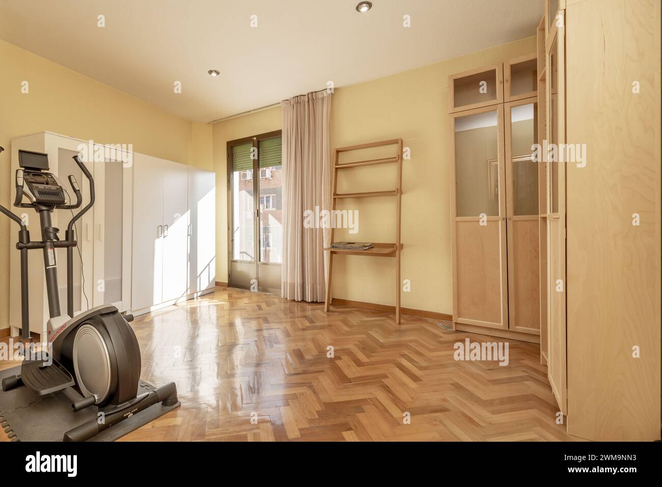 Zimmer mit ein paar Schränken an den Wänden, glänzend lackiertem Parkettboden und einem einsamen Trainingsgerät Stockfoto