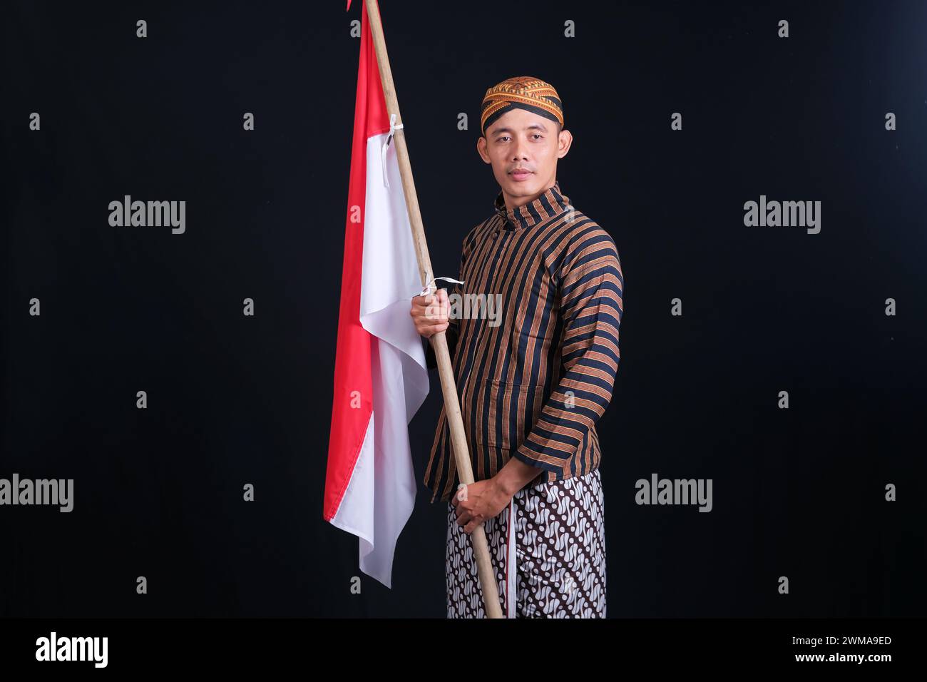 Junger Mann mit indonesischer Nationalflagge, der den Monat der Unabhängigkeit auf schwarzem Hintergrund begrüßt Stockfoto