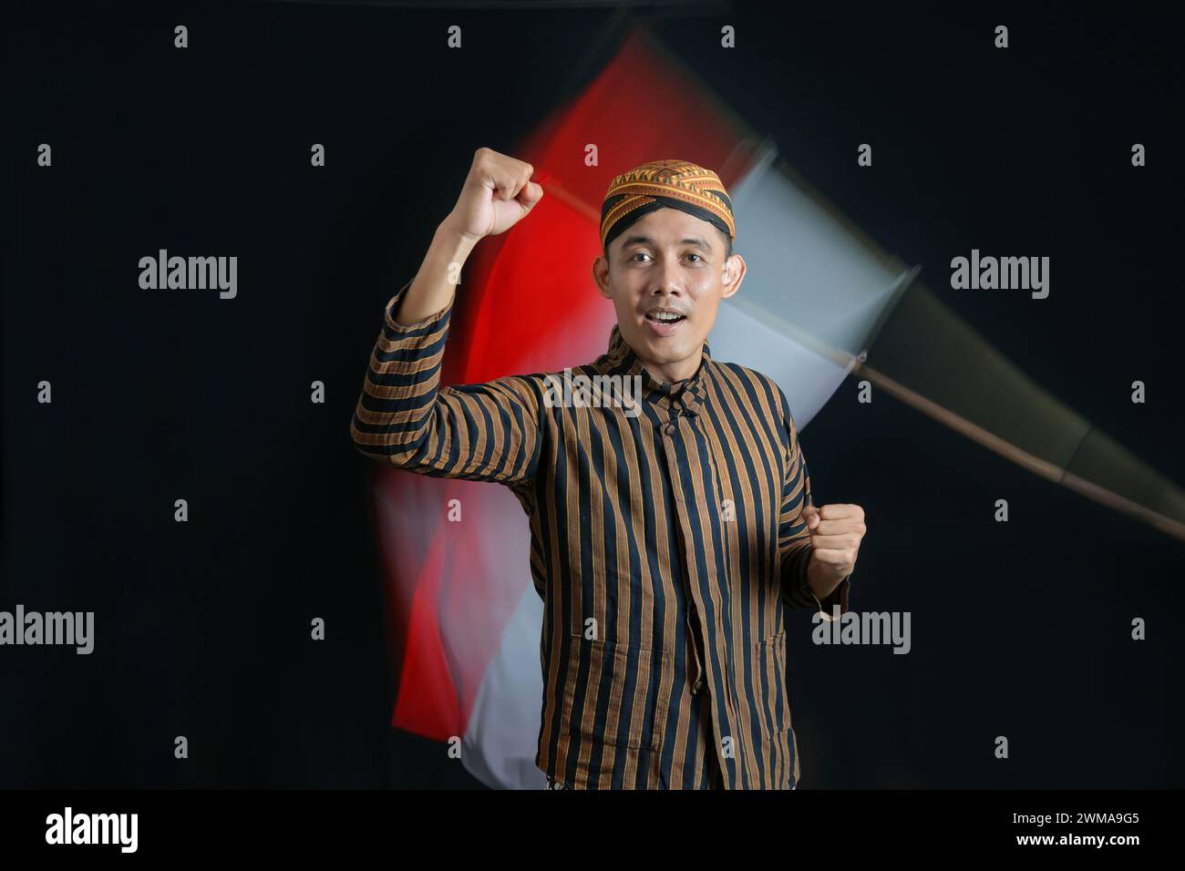 Junger Mann mit indonesischer Nationalflagge, der den Monat der Unabhängigkeit auf schwarzem Hintergrund begrüßt Stockfoto