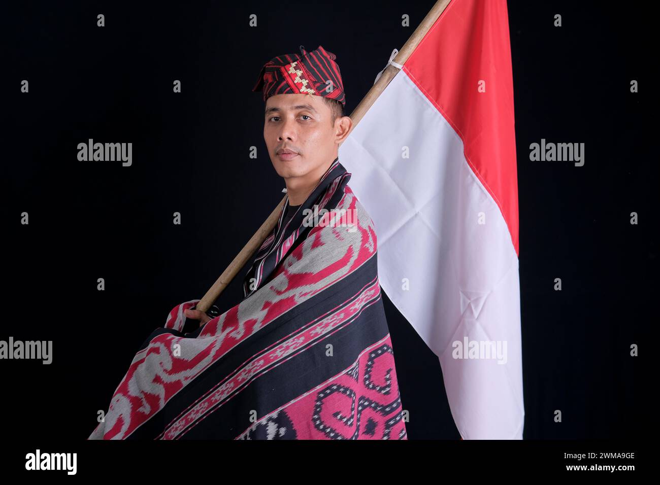 Mann, der traditionelle gewebte Kleidung trägt und indonesische Nationalflagge in Unabhängigkeit hält, isoliert auf weißem Hintergrund Stockfoto