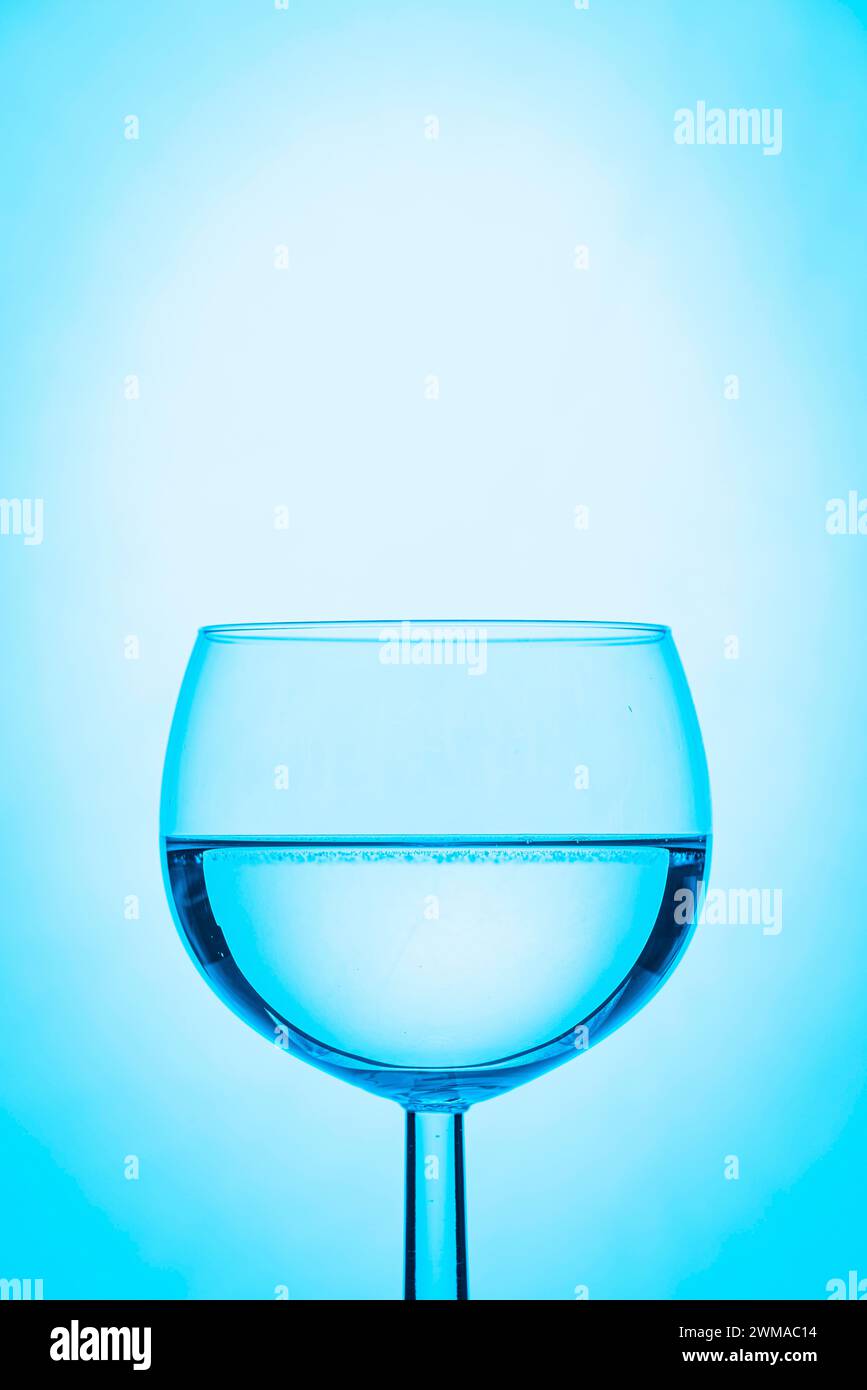 Weinglas halb gefüllt mit Wasser und blauem Hintergrund Stockfoto