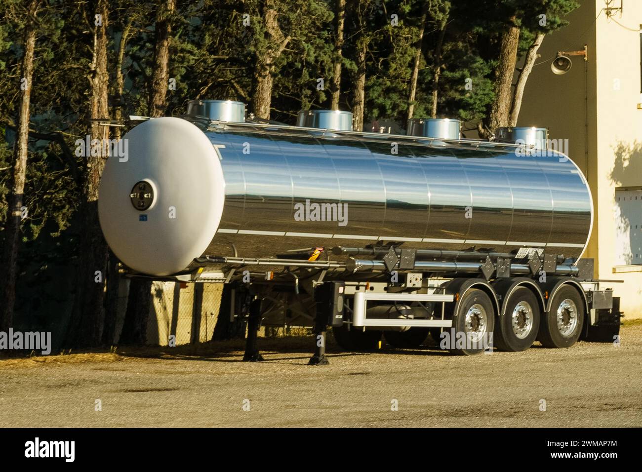 Ein Tankwagen aus Edelstahl steht auf einer Asphaltoberfläche, die in Sonnenlicht getaucht ist und wahrscheinlich transportbereit ist. Der Anhänger reflektiert seine Umgebung Stockfoto