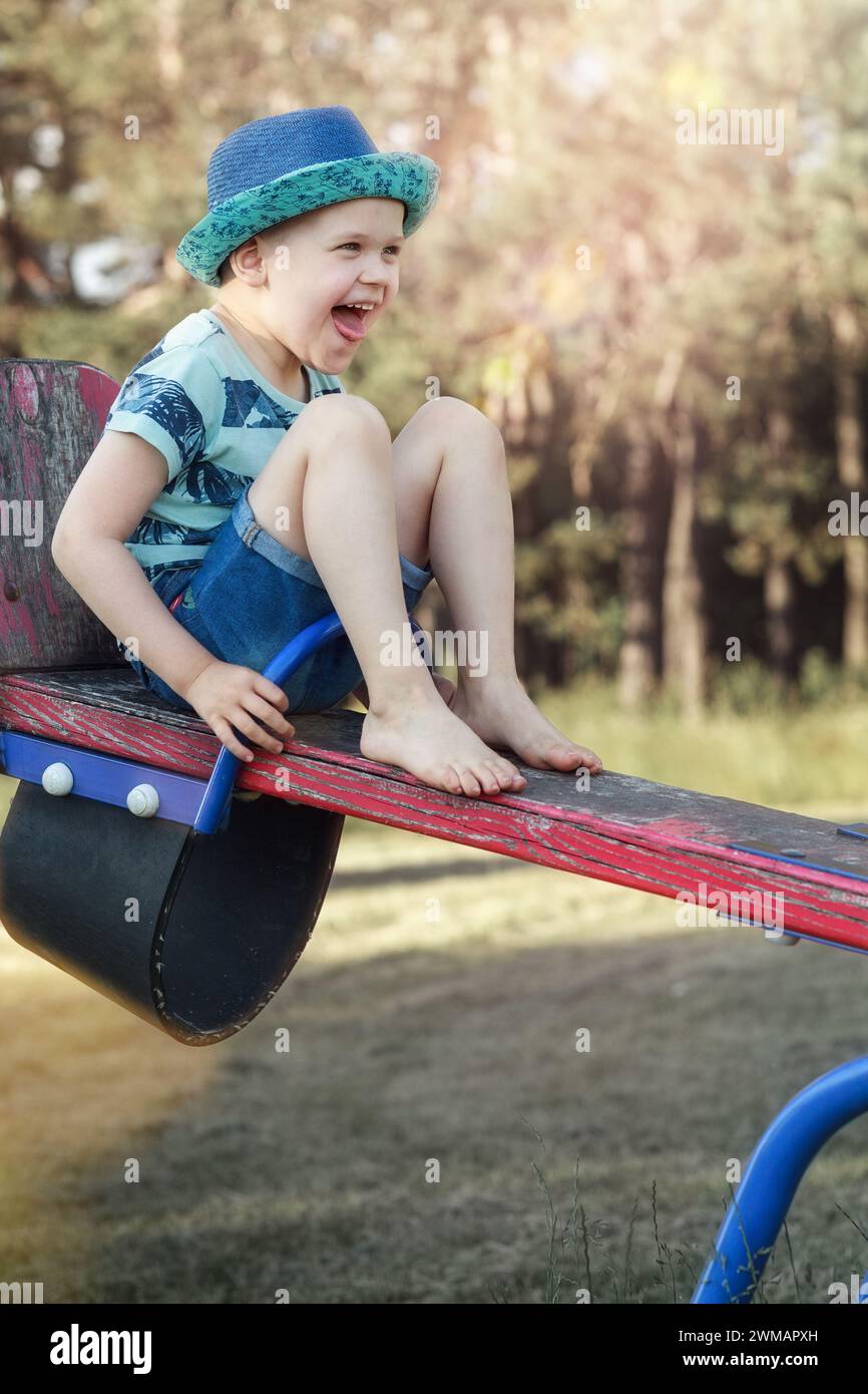 Ein kleiner Junge auf einer Balance, der hochgehoben wird, ist sehr glücklich und lacht. Stockfoto
