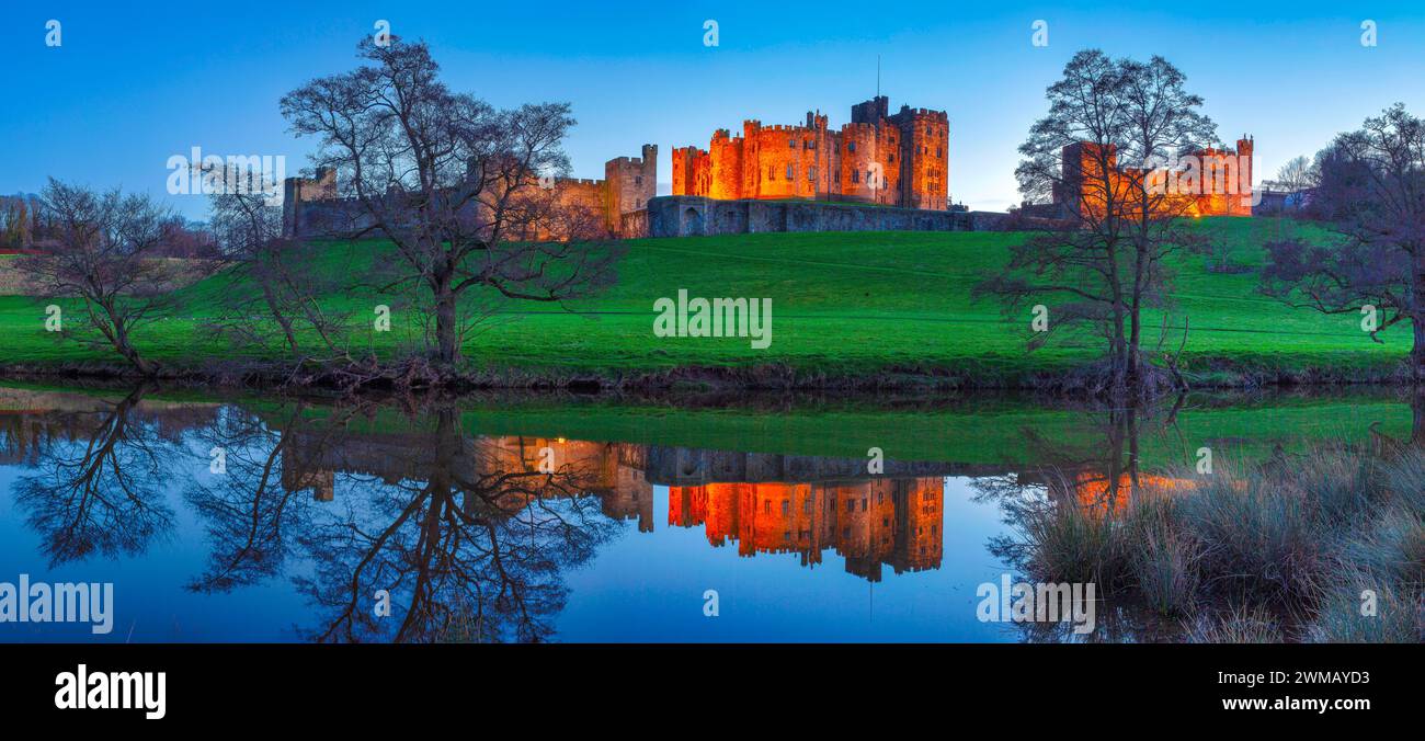 Blick auf Alnwick Castle in Northumberland, beleuchtet bei Nacht, während sie im Fluss ALN von den Weiden aus gesehen reflektiert wird Stockfoto