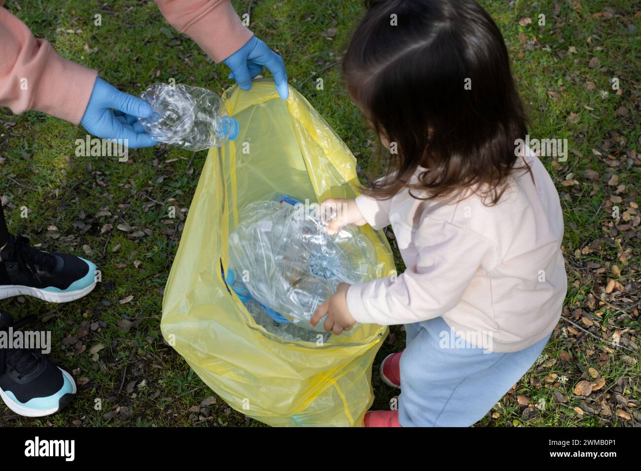 Die junge Mutter mit ihrer Tochter recycelt Plastikflaschen und steckt sie in einen gelben Müllsack. Recycling-Konzept, Mutterschaft, Freiwilligenarbeit Stockfoto