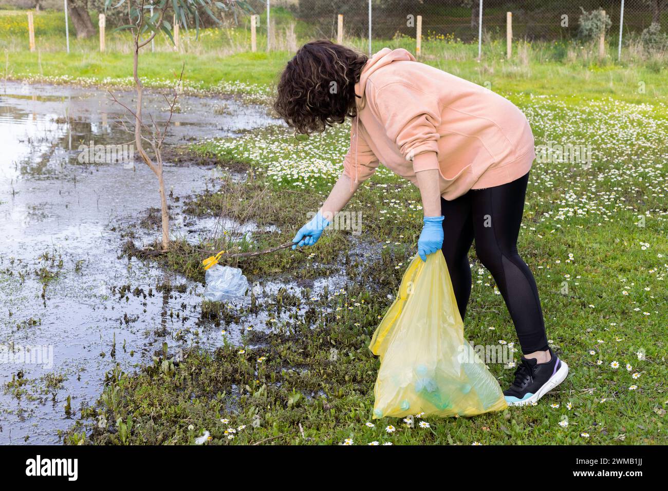 Eine junge Frau recycelt Plastikflaschen aus einem See an einem Recyclingtag. Konzept Recycling, Freiwilligenarbeit, Landschaftsgestaltung, Umwelt Stockfoto