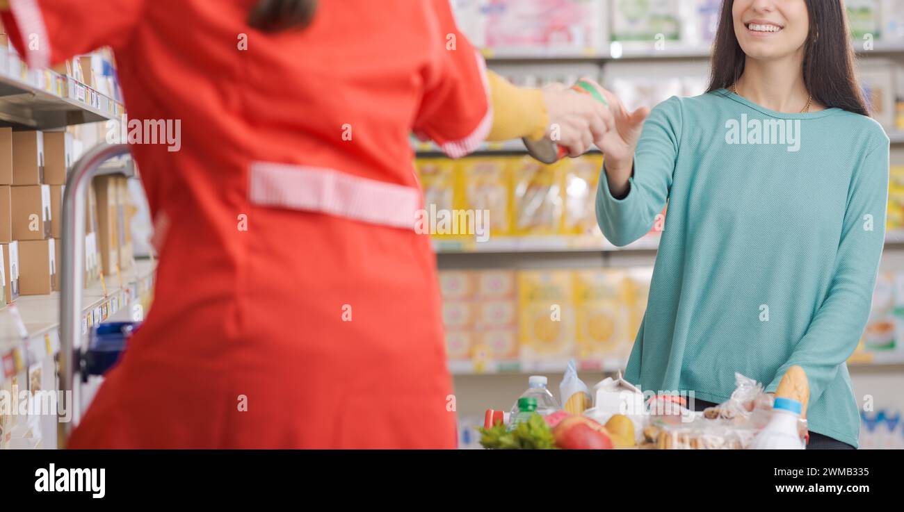 Die Verkäuferin hilft einem Kunden im Supermarkt und nimmt ein Produkt aus dem Regal und gibt es ihr Stockfoto