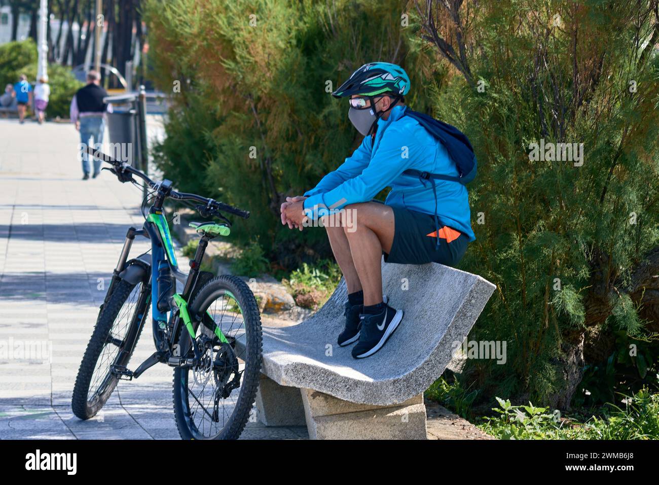 Vigo, Pontevedra, Spanien; 23. Juni 2021; MTB-Radfahrer mit Brille, Helm, Maske sitzt auf einer Bank neben seinem Fahrrad Stockfoto