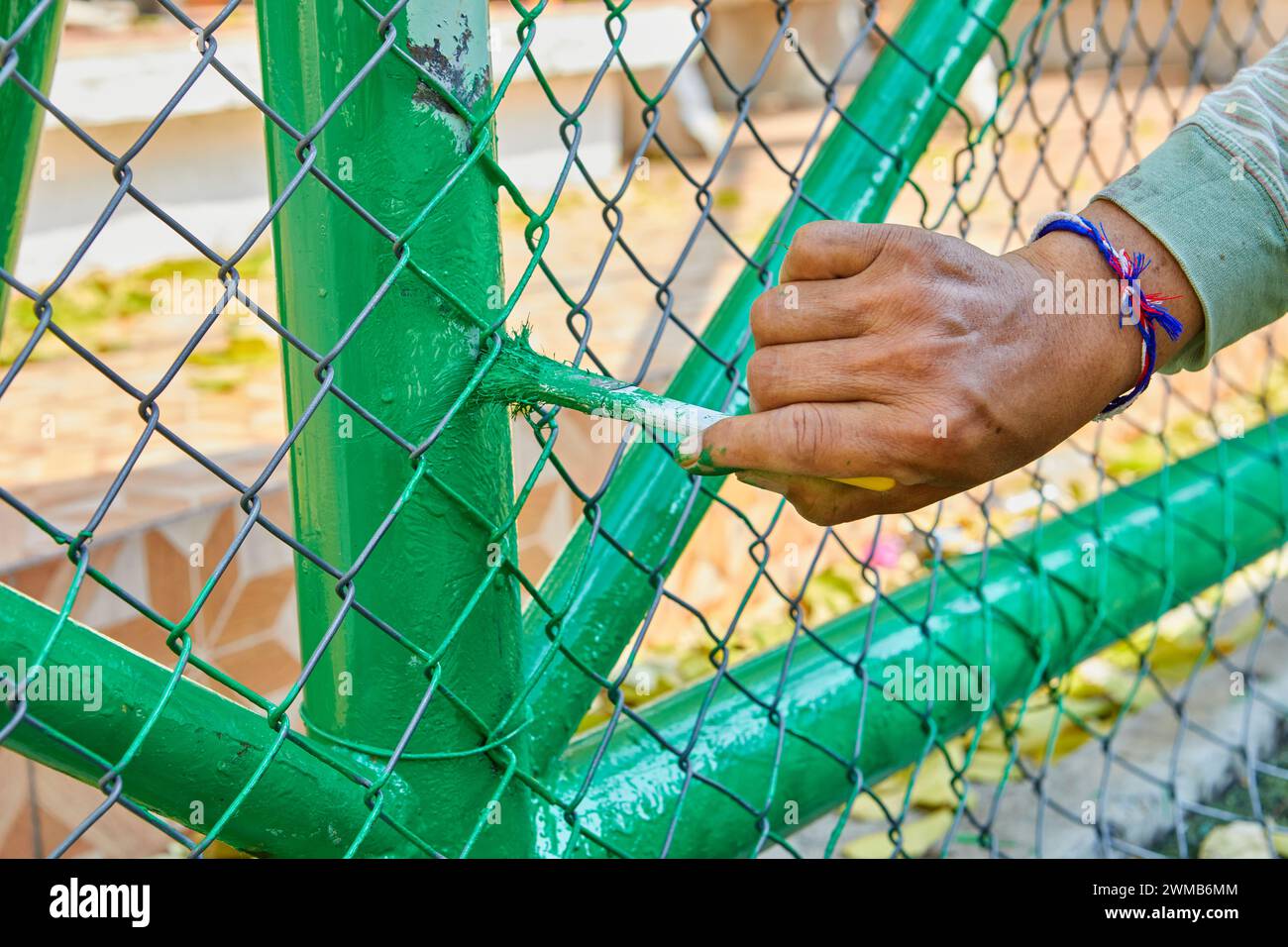 Abgeschnittene Hand eines Mannes, der Farbe auf den Kettengliedzaun malte Stockfoto