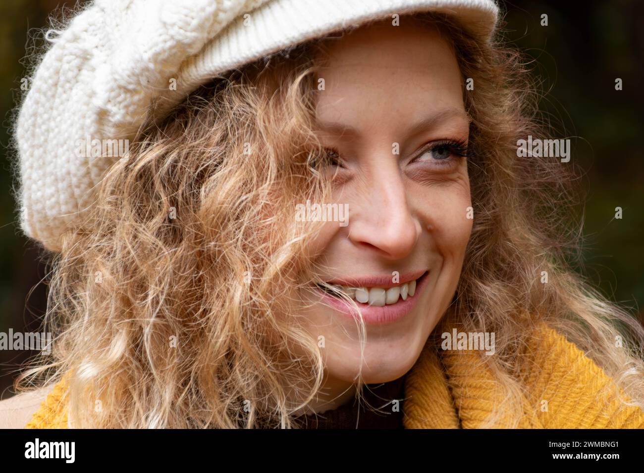 Nahaufnahme eines blonden Mädchens mit blauen Augen und lockigen Haaren. Weiße Wollmütze Stockfoto