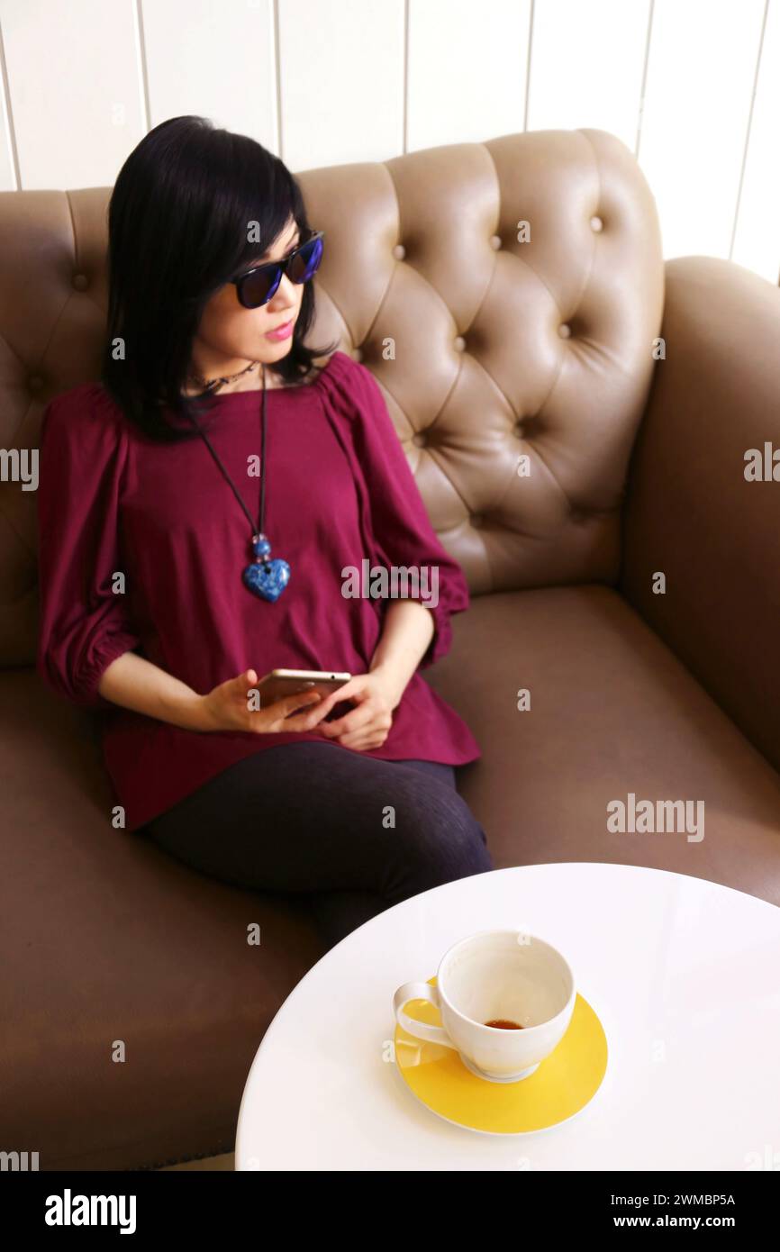 Frau, die auf einer Couch sitzt, mit einer leeren Kaffeetasse auf dem Tisch Stockfoto