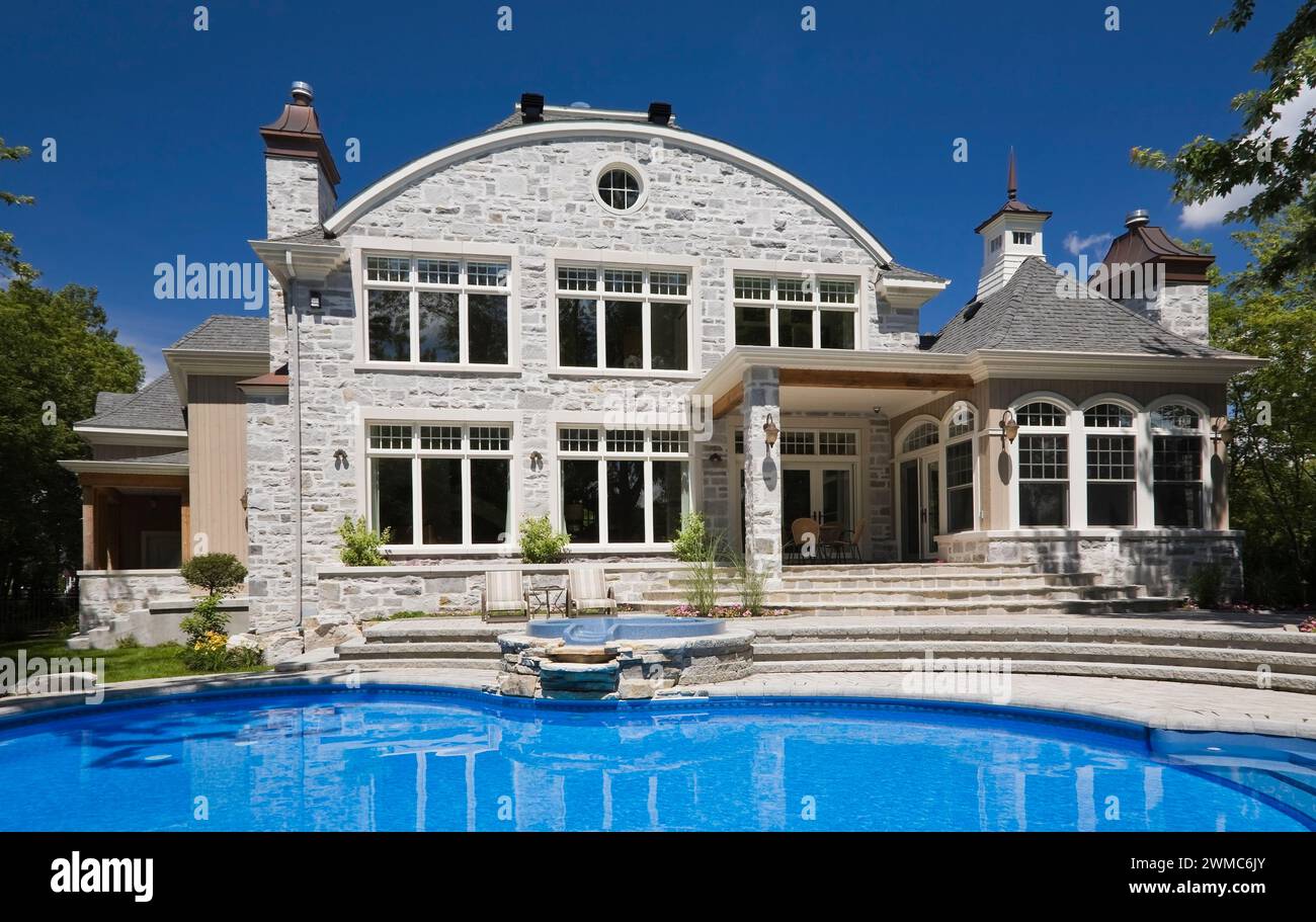 In-Ground Swimmingpool im Hinterhof eines luxuriösen zweistöckigen Natursteinhauses im Sommer. Stockfoto