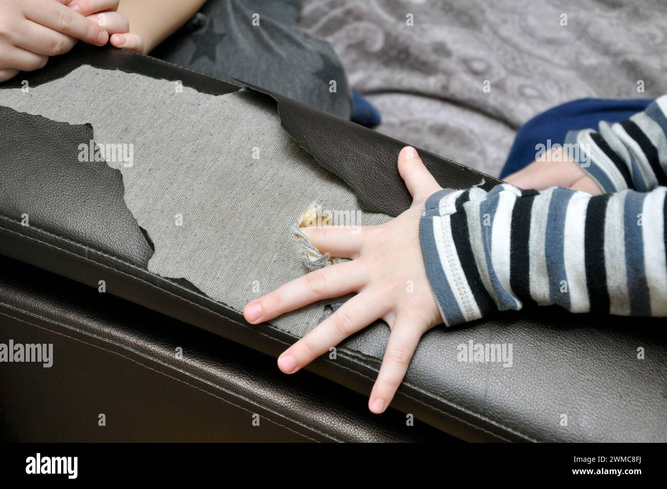 Kinderspiele verursachen Schäden an den Wohnmöbeln. Der Finger eines Kindes durchbohrt das Sofa und macht ein Loch darin. Stockfoto