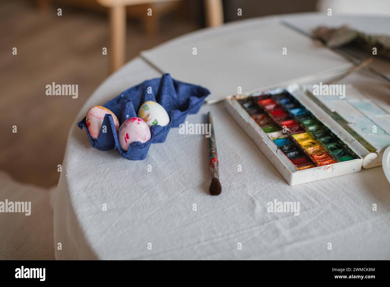 Nahaufnahme eines Pinsels, einer Farbpalette und eines Kartons mit Eiern, die für die Osterdekoration gemalt werden Stockfoto