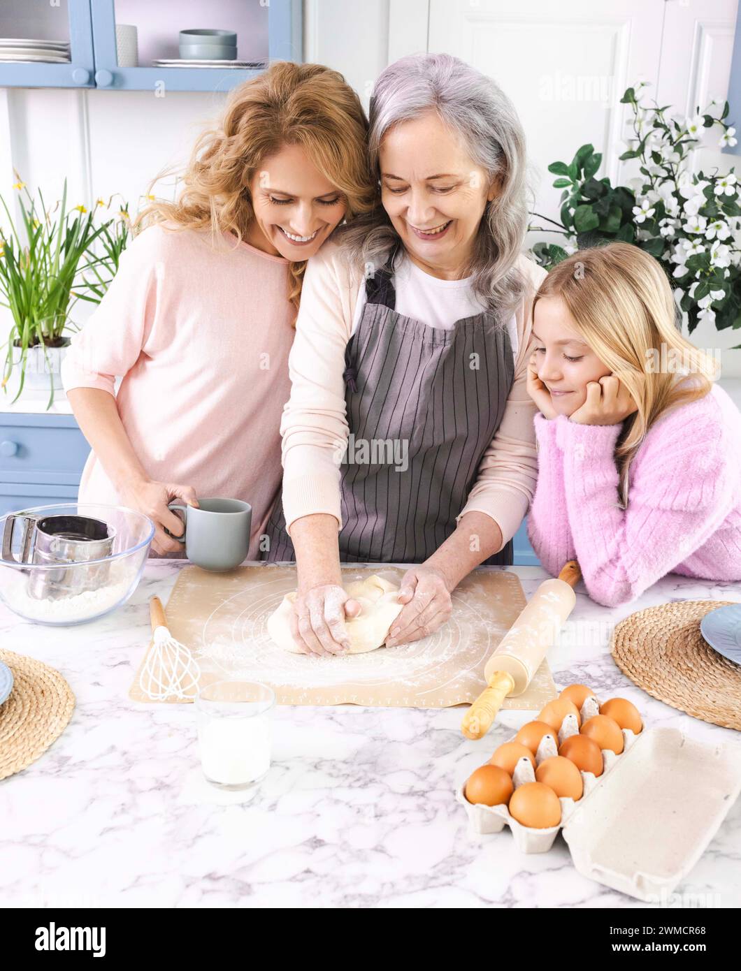 Oma, Mom und Enkelin verbinden sich beim Backen, Mehl, Eier und Milch mit Teig auf dem Küchentisch Stockfoto