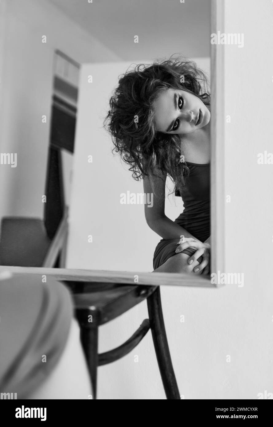 Porträt eines seltsamen, verrückten Mädchens. Gefährliche verrückte junge Frau, die auf dem Stuhl am Spiegel sitzt. Schwarz-weiß Stockfoto