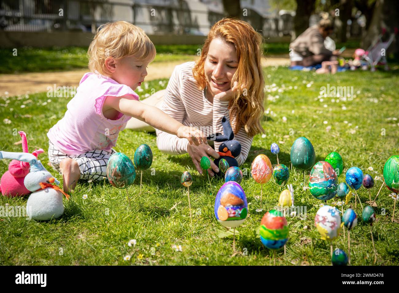 Mutter und kleine Tochter feiern frohe Ostern im Park am sonnigen Tag mit bemalten Eiern und Kaninchen Stockfoto
