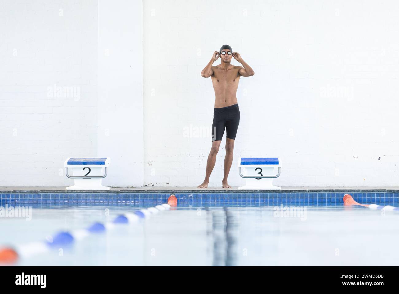 Junger männlicher Sportler passt seine Brille am Pool an Stockfoto