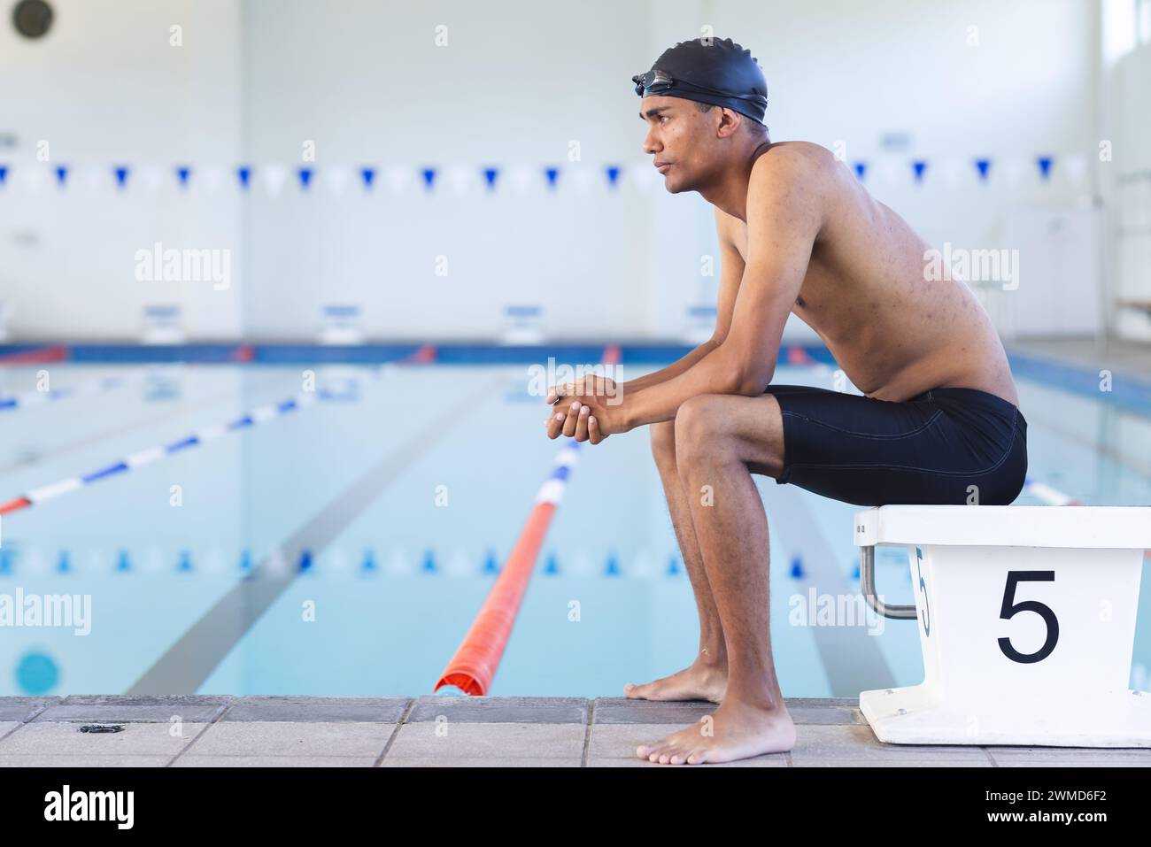Junger männlicher Sportler mit birassischem Charakter sitzt nachdenklich am Pool und hat Platz für Kopiergeräte Stockfoto