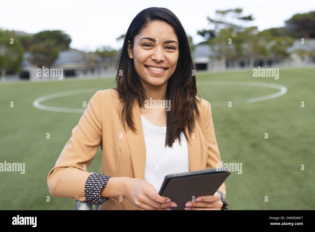 Der junge Lehrer lächelt und hält ein Tablet auf einem Sportplatz Stockfoto