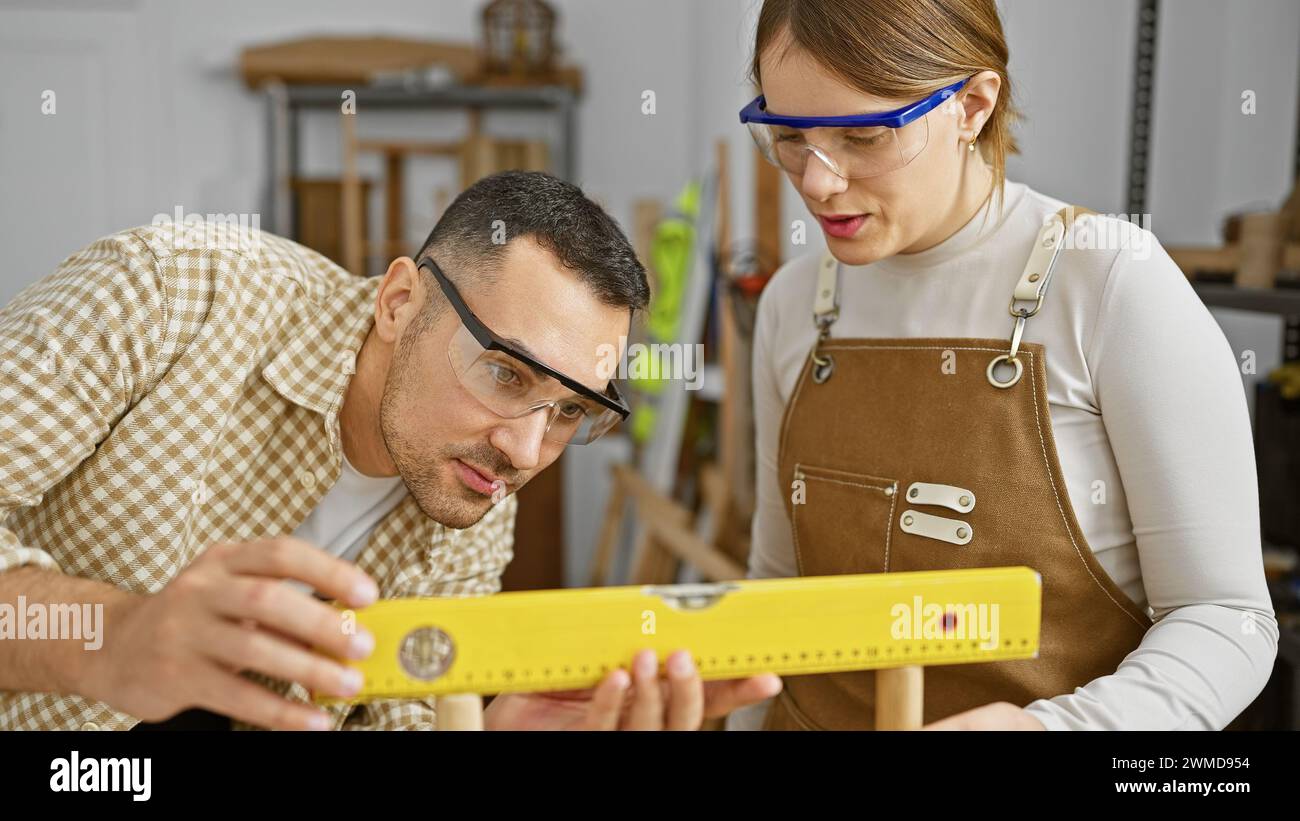 Ein Mann und eine Frau in Schutzbrille mit Fokus auf präzise Messungen mit gelbem Niveau in einer Holzwerkstatt. Stockfoto