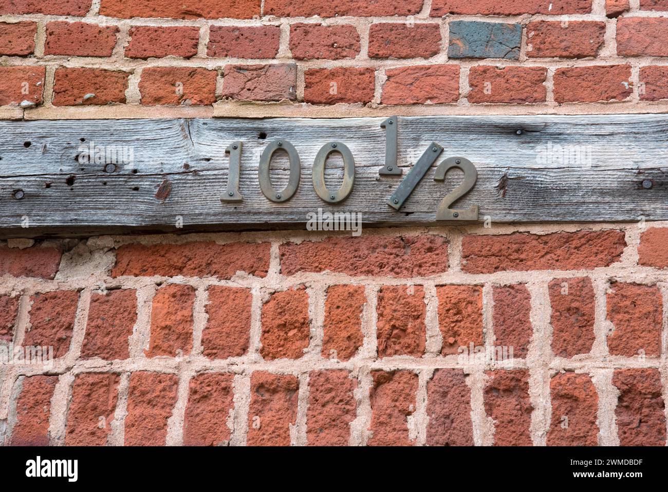 Altes und verwittertes hölzernes Adressschild mit Metallziffern, ungewöhnliche Nummer 100 1/2. Stockfoto