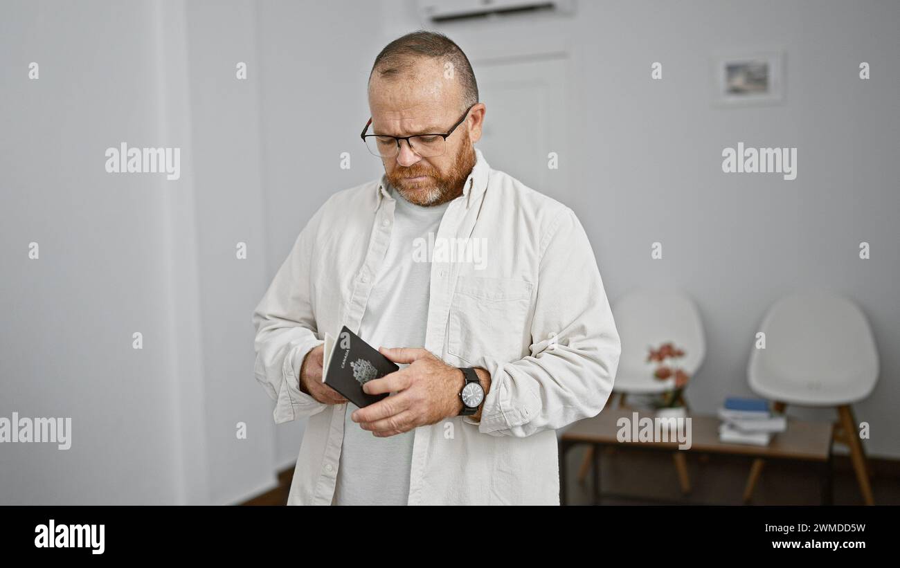 Gutaussehender kaukasier mittleren Alters, mit Bart und Brille, hält seinen Pass, in Gedanken getaucht, während er lässig im Wartezimmer steht, po Stockfoto