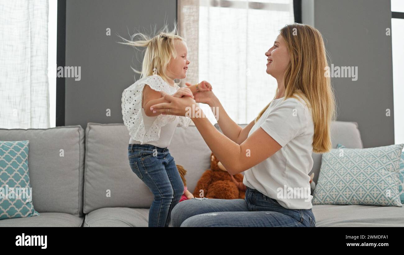 Selbstbewusste kaukasische Mutter und Tochter kichern, während sie auf das Sofa springen und Freude in ihrem entspannten Zuhause ausstrahlen Stockfoto