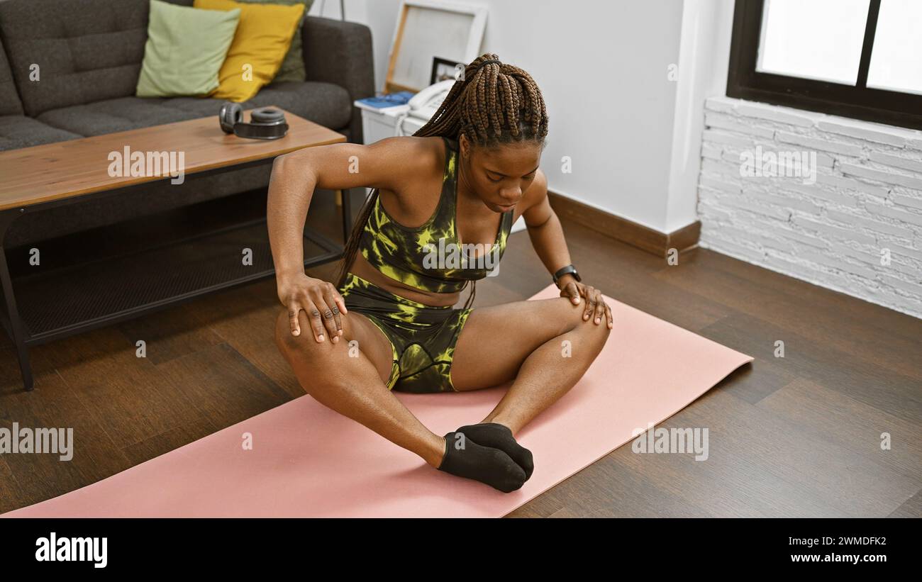 afroamerikanische Frau, die sich auf einer Yogamatte in einem gemütlichen Wohnzimmer ausdehnt und Fitness und einen gesunden Lebensstil darstellt. Stockfoto