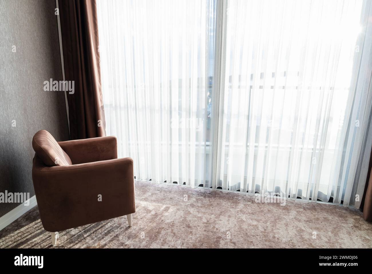 An einem sonnigen Tag steht ein komfortabler Luxussessel in einem leeren Raum vor dem Panoramafenster Stockfoto