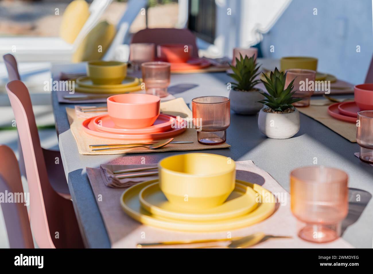 Stellen Sie den Esstisch im Freien mit farbenfrohen Schüsseln, Tellern, Gläsern und Besteck Stockfoto