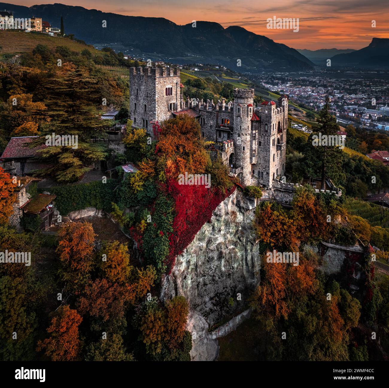 Merano, Italien - Panoramablick aus der Vogelperspektive auf das berühmte Schloss Brunnenburg (Castel Tirolo) mit der Stadt Merano, den italienischen Dolomiten und der bunten Sonne Stockfoto