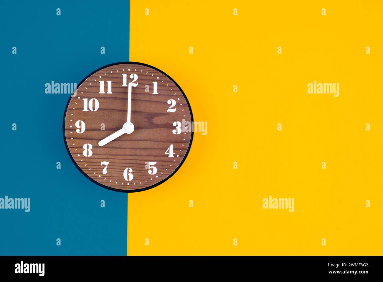 Hölzerne Uhr auf blauem und gelbem Hintergrund, Position mit Kopierraum. Stockfoto