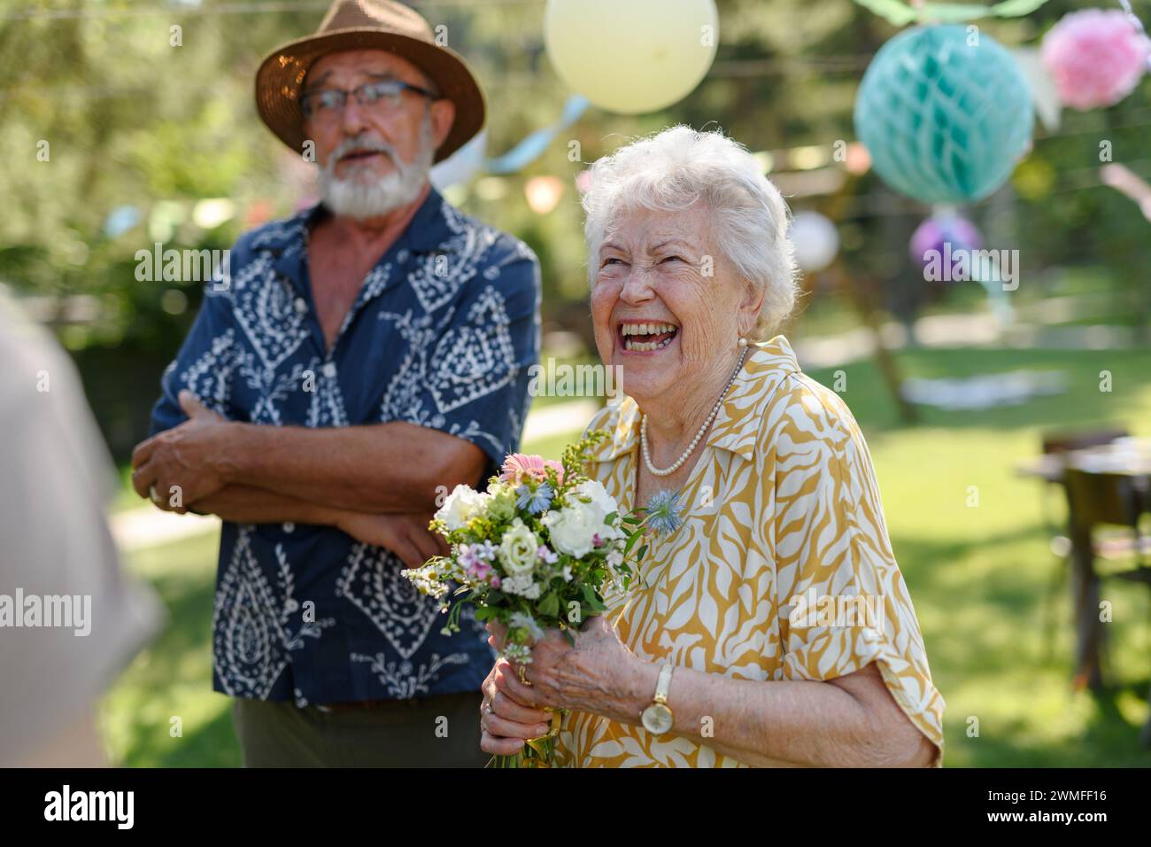 Schöne ältere Geburtstagsfrau, die Blumen als Geschenk erhält. Gartengeburtstag für Seniorin. Stockfoto