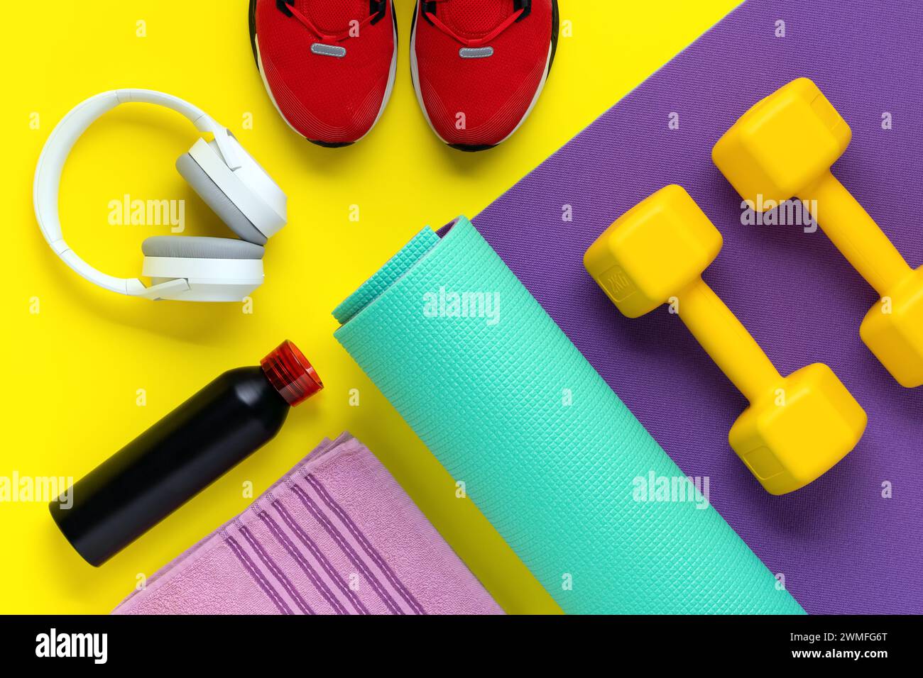 Fitnessgeräte. Sporttrainingskonzept. Kurzhanteln auf lila Rollenmatte auf gelbem Hintergrund. Gesunder Lebensstil. Flache Lagen. Rote Sneakers, Musik-Headpho Stockfoto