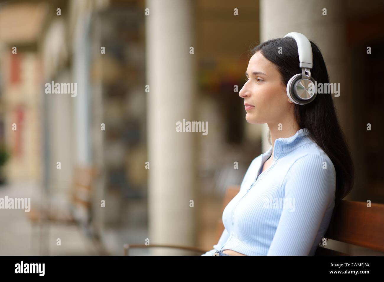 Seitliches Porträt einer ernsten Frau, die Audio mit Kopfhörern auf der Straße hört Stockfoto