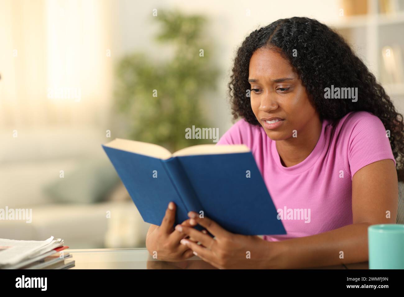 Eine ekelhafte schwarze Frau, die zu Hause ein Papierbuch liest Stockfoto