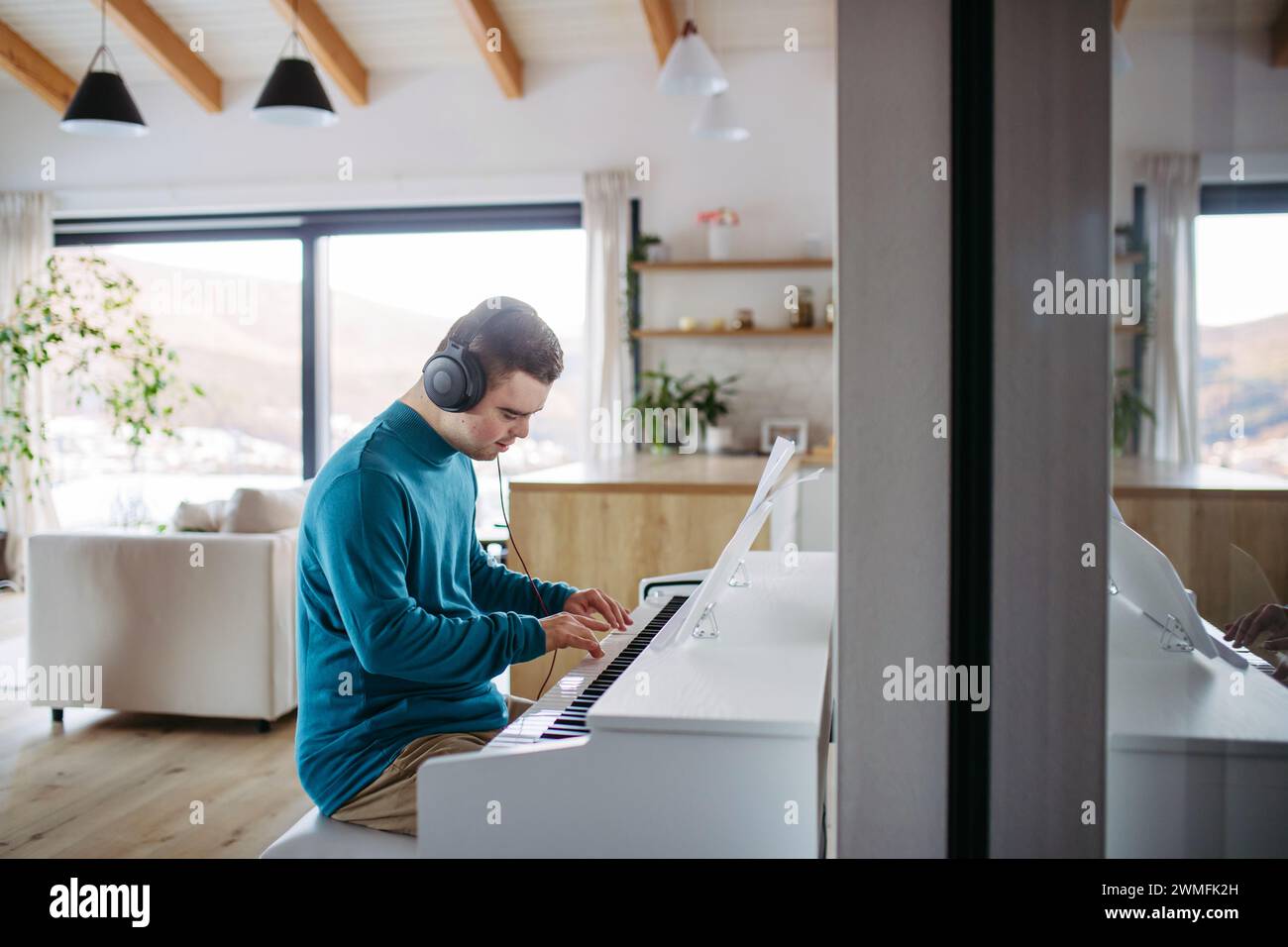 Junger Mann mit Down-Syndrom, der am Klavier spielt und seine Musik über Kopfhörer hört. Stockfoto