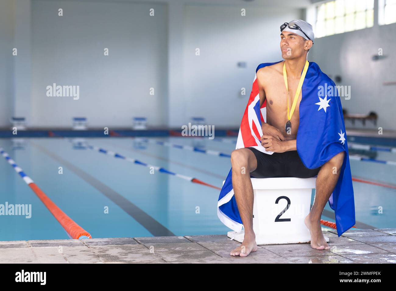 Der Schwimmer, der in eine australische Flagge gewickelt ist, sitzt am Pool mit einer Medaille und einem Kopierraum Stockfoto