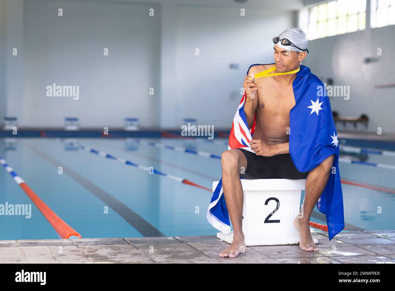 Ein junger männlicher Schwimmer mit australischer Flagge sitzt am Pool mit einer Medaille Stockfoto