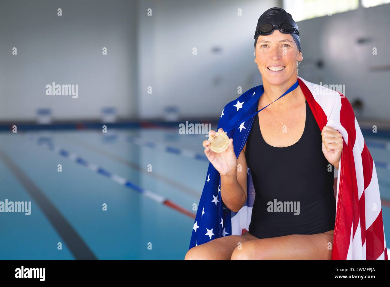 Die weiße Frau zeigt ihre Goldmedaille am Pool mit einer amerikanischen Flagge Stockfoto