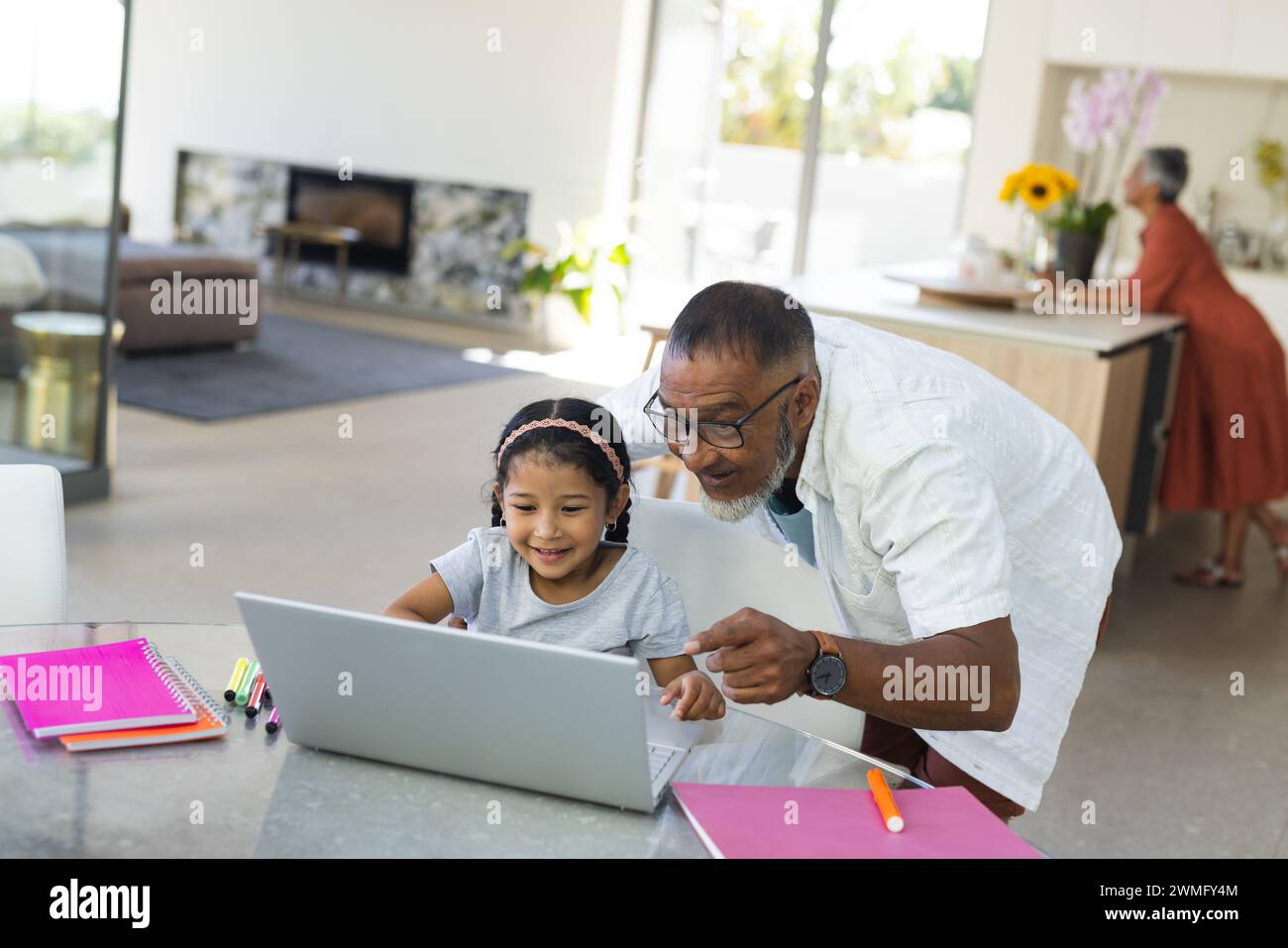 Der birassische Großvater hilft einer jungen Enkelin mit einem Laptop bei der Schularbeit zu Hause Stockfoto