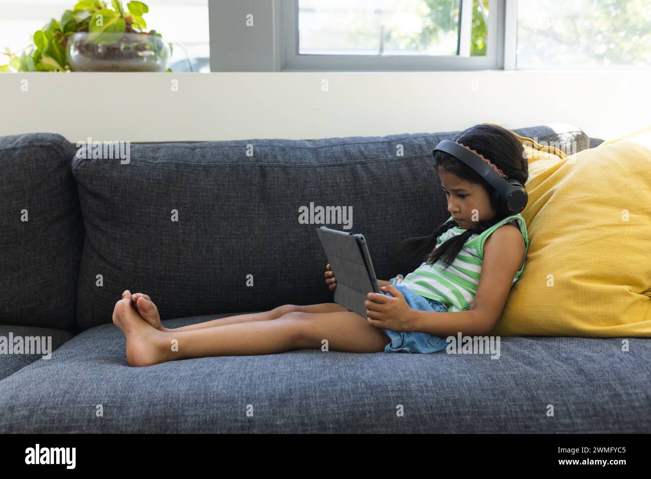 Biracial Girl genießt ein Tablet auf einem gemütlichen Sofa zu Hause mit Kopierraum Stockfoto